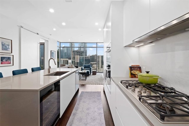 kitchen with a kitchen bar, sink, white cabinetry, appliances with stainless steel finishes, and expansive windows