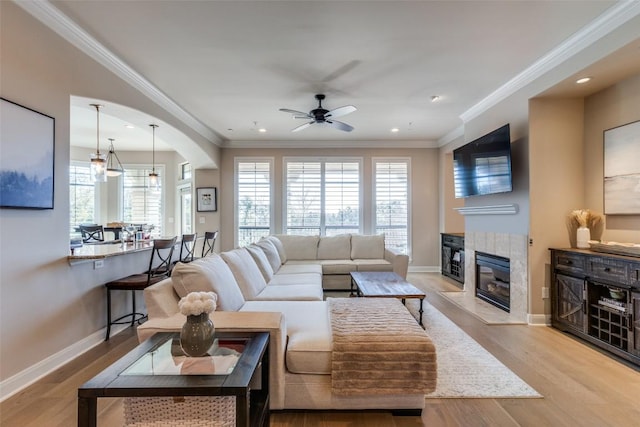 living room featuring a tile fireplace, ornamental molding, ceiling fan, and light wood-type flooring