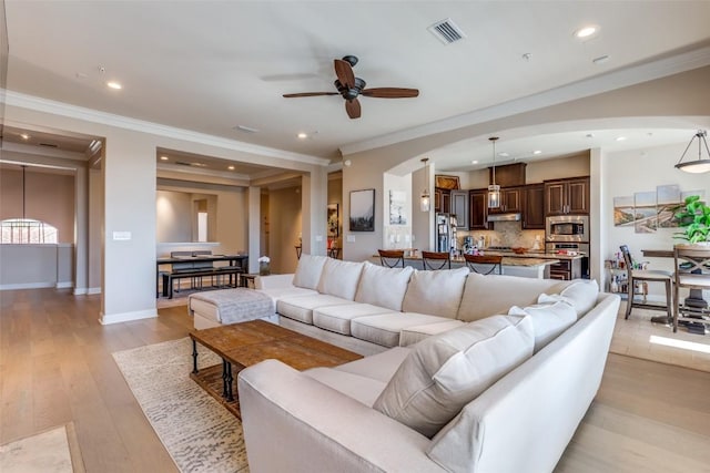 living room with ceiling fan, ornamental molding, and light wood-type flooring