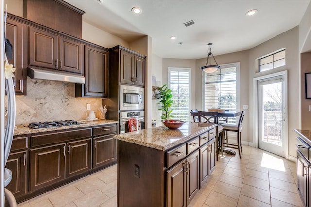 kitchen featuring a center island, appliances with stainless steel finishes, dark brown cabinets, and decorative light fixtures