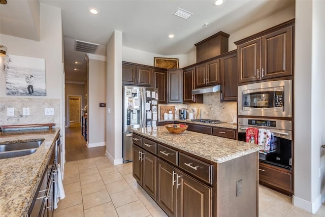 kitchen with light stone counters, dark brown cabinets, a kitchen island, and appliances with stainless steel finishes