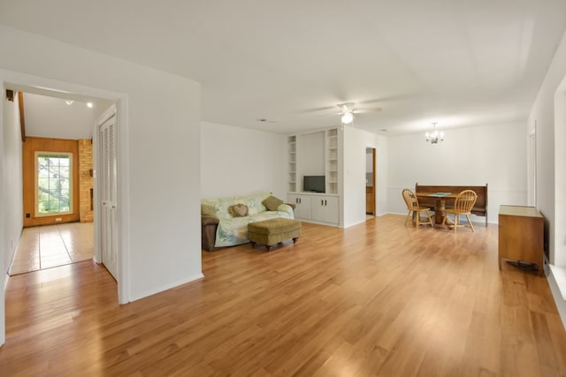 sitting room featuring built in features, ceiling fan with notable chandelier, and light hardwood / wood-style flooring