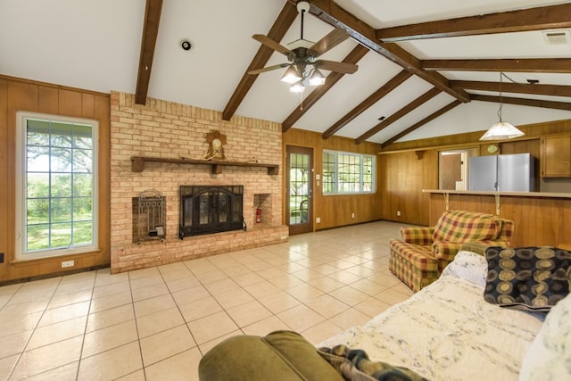 unfurnished living room featuring ceiling fan, vaulted ceiling with beams, light tile patterned flooring, a brick fireplace, and wood walls