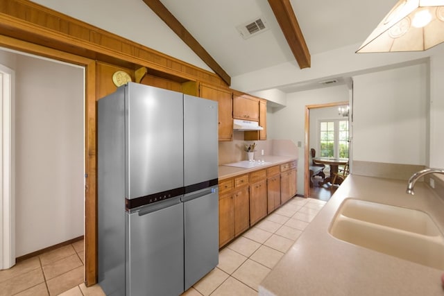 kitchen with light tile patterned flooring, sink, vaulted ceiling with beams, and stainless steel fridge