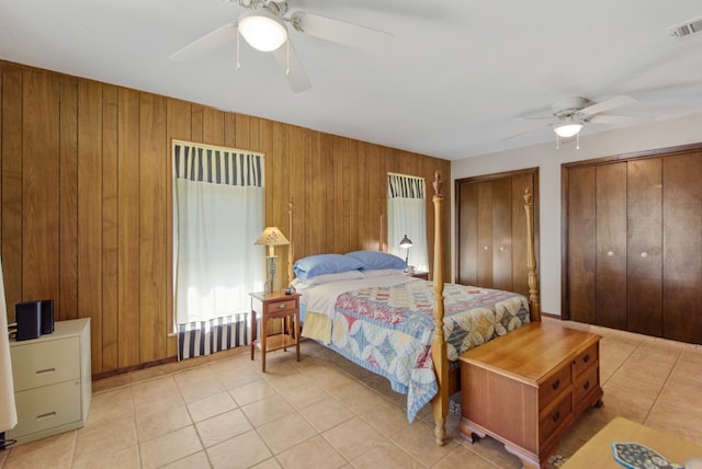 tiled bedroom with ceiling fan, wooden walls, and multiple closets