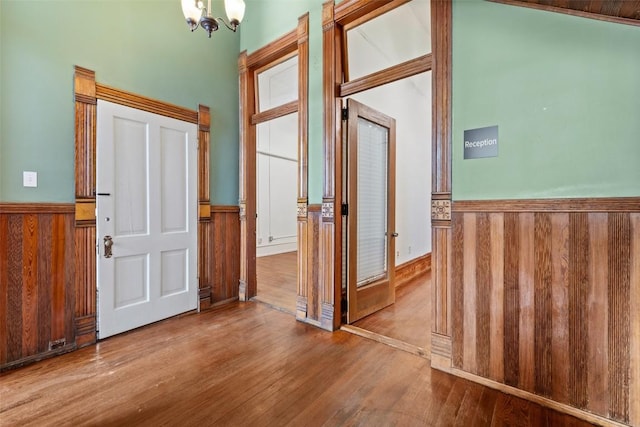 entryway featuring wood-type flooring, wooden walls, and an inviting chandelier