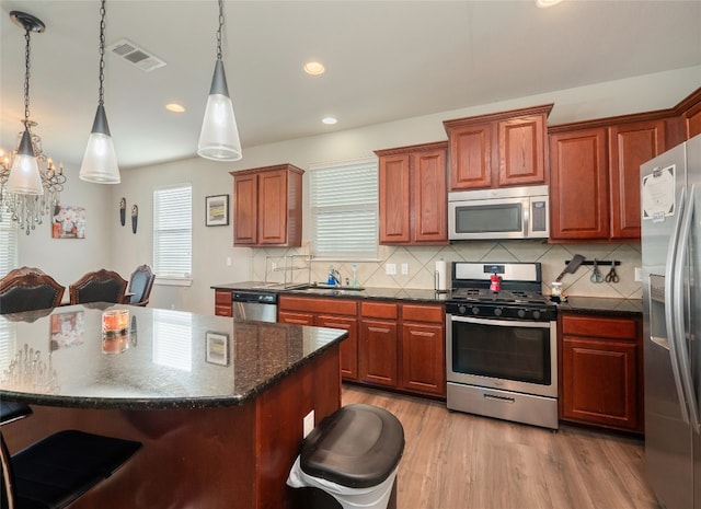 kitchen featuring stainless steel appliances, a center island, a kitchen bar, and decorative light fixtures