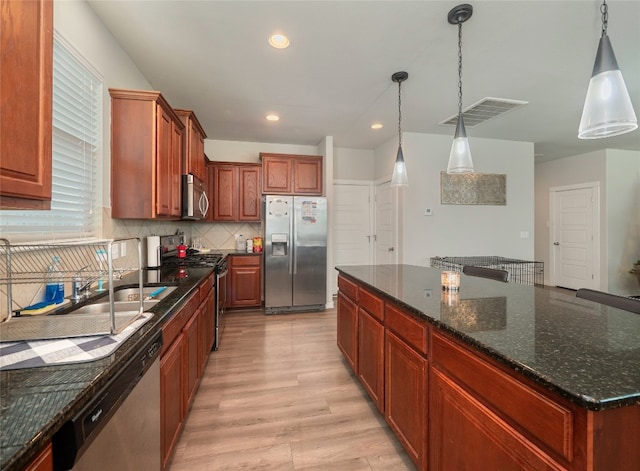 kitchen featuring decorative light fixtures, light hardwood / wood-style flooring, appliances with stainless steel finishes, a kitchen island, and decorative backsplash