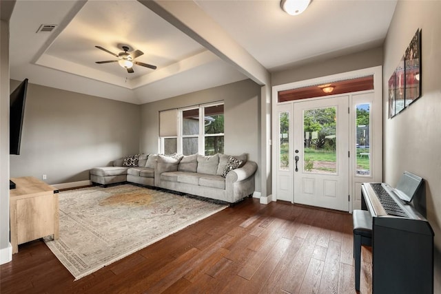 living room with dark wood-type flooring, ceiling fan, and a tray ceiling