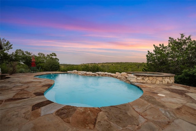 pool at dusk with an in ground hot tub and a patio