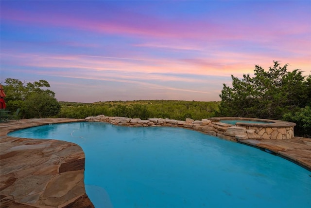 pool at dusk with an in ground hot tub