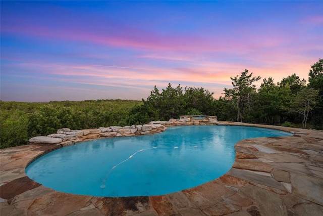 pool at dusk with a patio area and an in ground hot tub