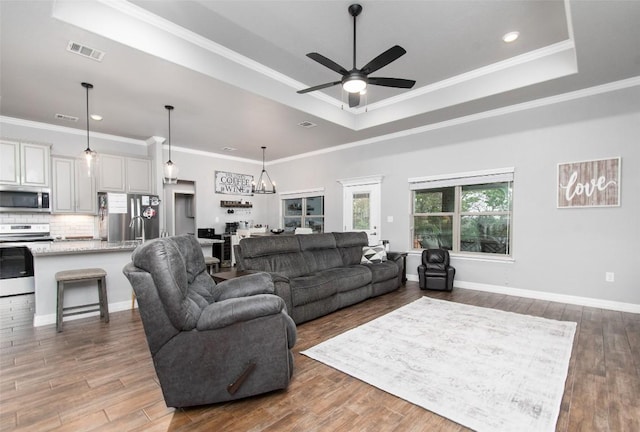 living room with crown molding, a tray ceiling, dark wood-type flooring, and ceiling fan with notable chandelier