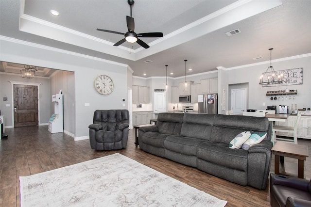 living room with ornamental molding, dark hardwood / wood-style floors, ceiling fan with notable chandelier, and a tray ceiling