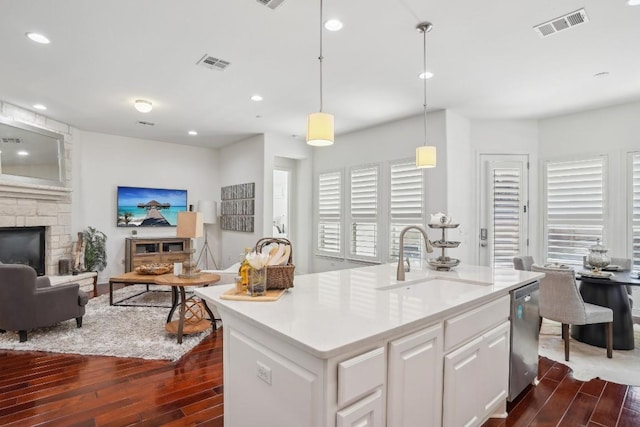 kitchen featuring sink, dishwasher, a kitchen island with sink, white cabinetry, and decorative light fixtures