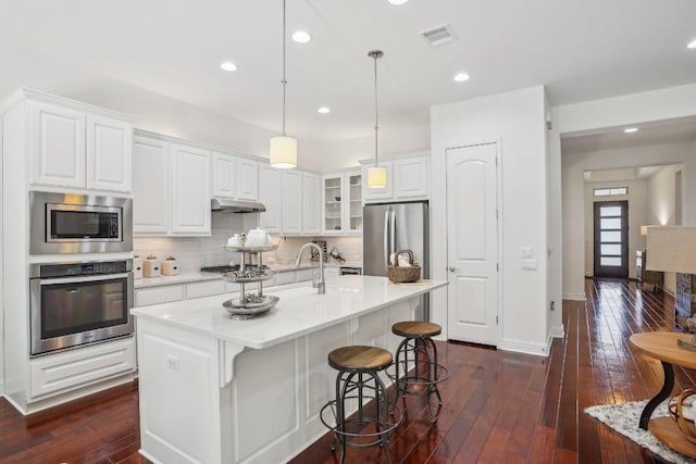 kitchen with white cabinetry, hanging light fixtures, a center island with sink, appliances with stainless steel finishes, and dark hardwood / wood-style floors