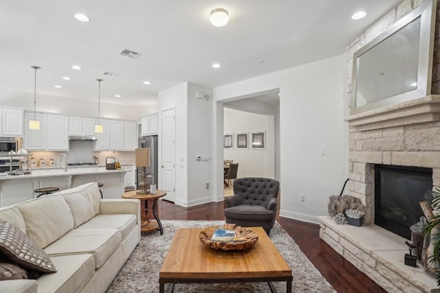 living room with a stone fireplace and dark hardwood / wood-style floors