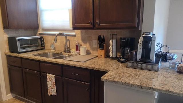 kitchen with tasteful backsplash, dark brown cabinetry, sink, and light stone counters