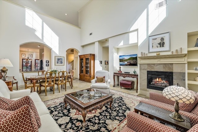 living room with ornamental molding, a tiled fireplace, and a high ceiling