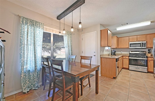 kitchen featuring light tile patterned flooring, appliances with stainless steel finishes, sink, hanging light fixtures, and a textured ceiling