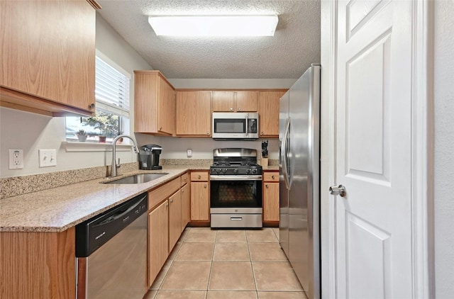 kitchen with light brown cabinetry, sink, light tile patterned floors, stainless steel appliances, and a textured ceiling