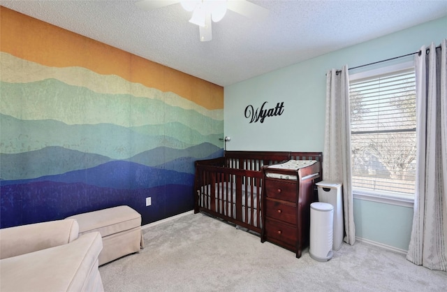 carpeted bedroom with a nursery area, ceiling fan, and a textured ceiling