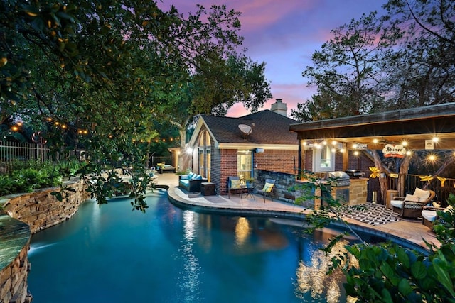 pool at dusk with exterior kitchen and a patio area