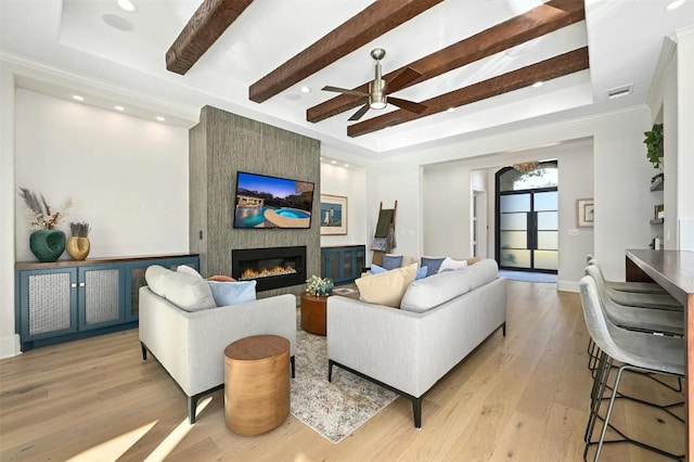 living room with light wood-type flooring, a large fireplace, a raised ceiling, beamed ceiling, and ceiling fan