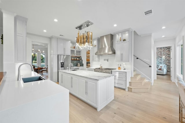 kitchen featuring pendant lighting, sink, a kitchen island with sink, white cabinetry, and wall chimney exhaust hood