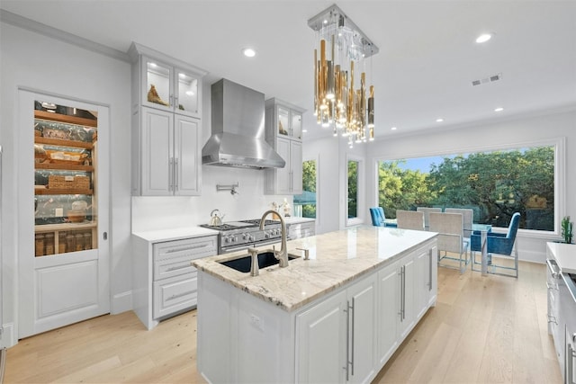 kitchen with white cabinetry, hanging light fixtures, a kitchen island with sink, light stone countertops, and wall chimney exhaust hood