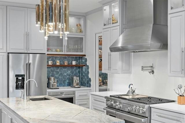 kitchen featuring high end appliances, white cabinets, light stone counters, and wall chimney range hood