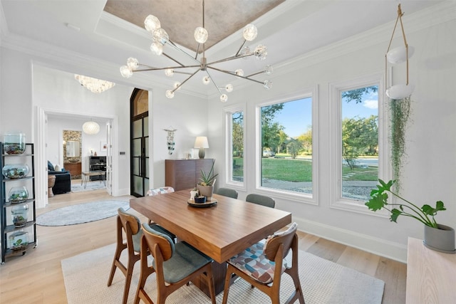 dining area with an inviting chandelier, a tray ceiling, ornamental molding, and light wood-type flooring