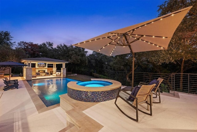 pool at dusk featuring an in ground hot tub, an outbuilding, and a patio area