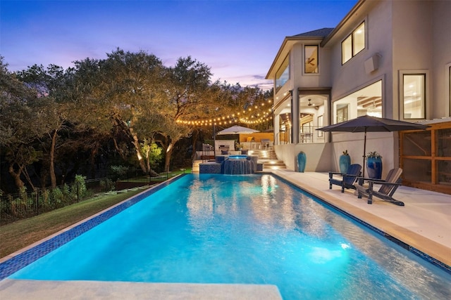 pool at dusk with an in ground hot tub, pool water feature, and a patio area