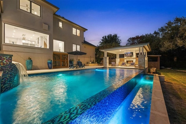 pool at dusk with a patio area and pool water feature