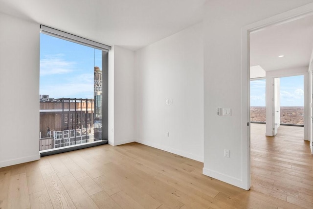 unfurnished room with a wall of windows and light hardwood / wood-style floors