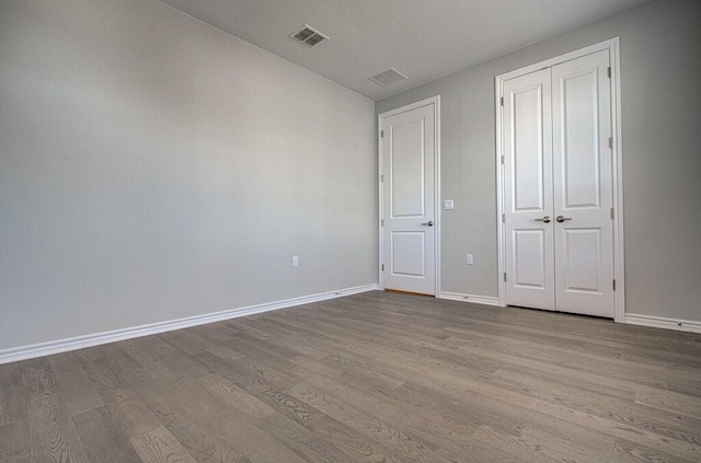 unfurnished bedroom featuring visible vents, a closet, baseboards, and wood finished floors