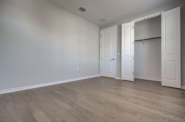 unfurnished bedroom with a closet, visible vents, baseboards, and wood finished floors