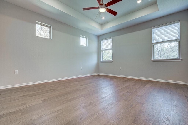 unfurnished room with ceiling fan, recessed lighting, wood finished floors, baseboards, and a tray ceiling