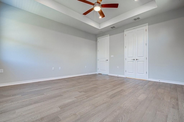 unfurnished bedroom with light wood finished floors, visible vents, a tray ceiling, and baseboards