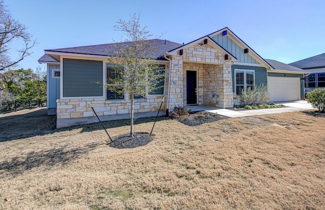 view of front of property featuring board and batten siding, a front yard, stone siding, and an attached garage