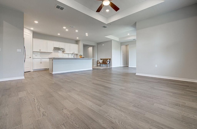 unfurnished living room with a ceiling fan, visible vents, light wood-style floors, and baseboards