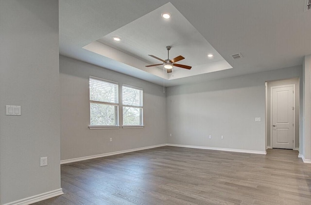 spare room with ceiling fan, wood finished floors, visible vents, baseboards, and a raised ceiling