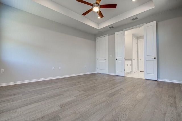 unfurnished bedroom featuring wood finished floors, a raised ceiling, visible vents, and baseboards