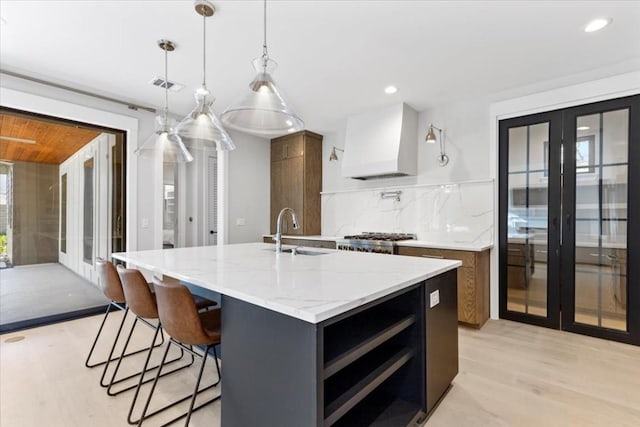 kitchen with french doors, sink, an island with sink, custom range hood, and pendant lighting