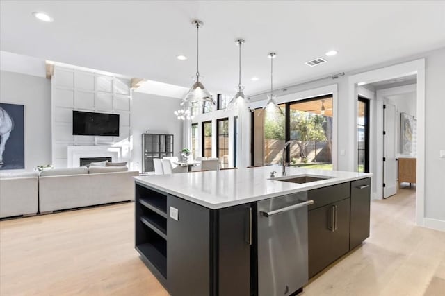 kitchen with pendant lighting, sink, stainless steel dishwasher, a center island with sink, and light wood-type flooring