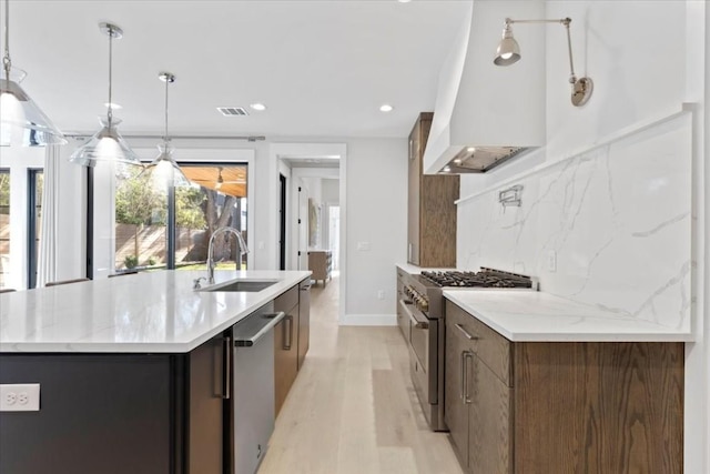 kitchen featuring sink, decorative light fixtures, a center island with sink, appliances with stainless steel finishes, and decorative backsplash