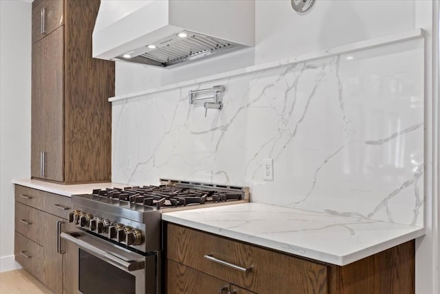 kitchen featuring premium range hood, stainless steel range, light stone countertops, and decorative backsplash