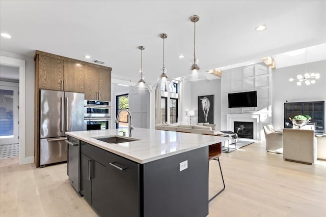 kitchen with sink, decorative light fixtures, a center island with sink, light wood-type flooring, and stainless steel appliances