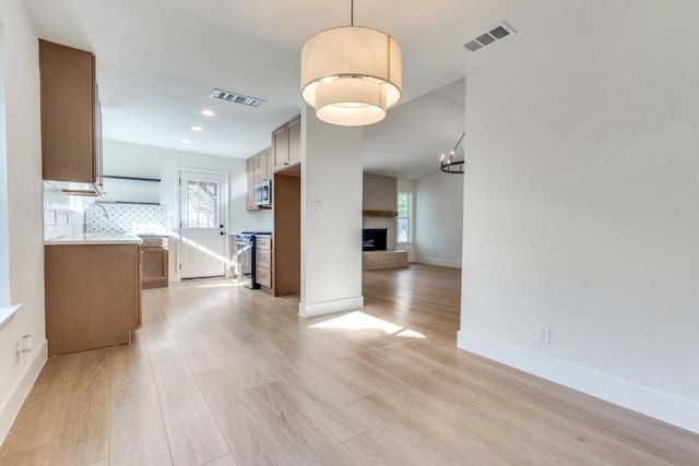 unfurnished dining area featuring a brick fireplace, a wealth of natural light, and light hardwood / wood-style flooring